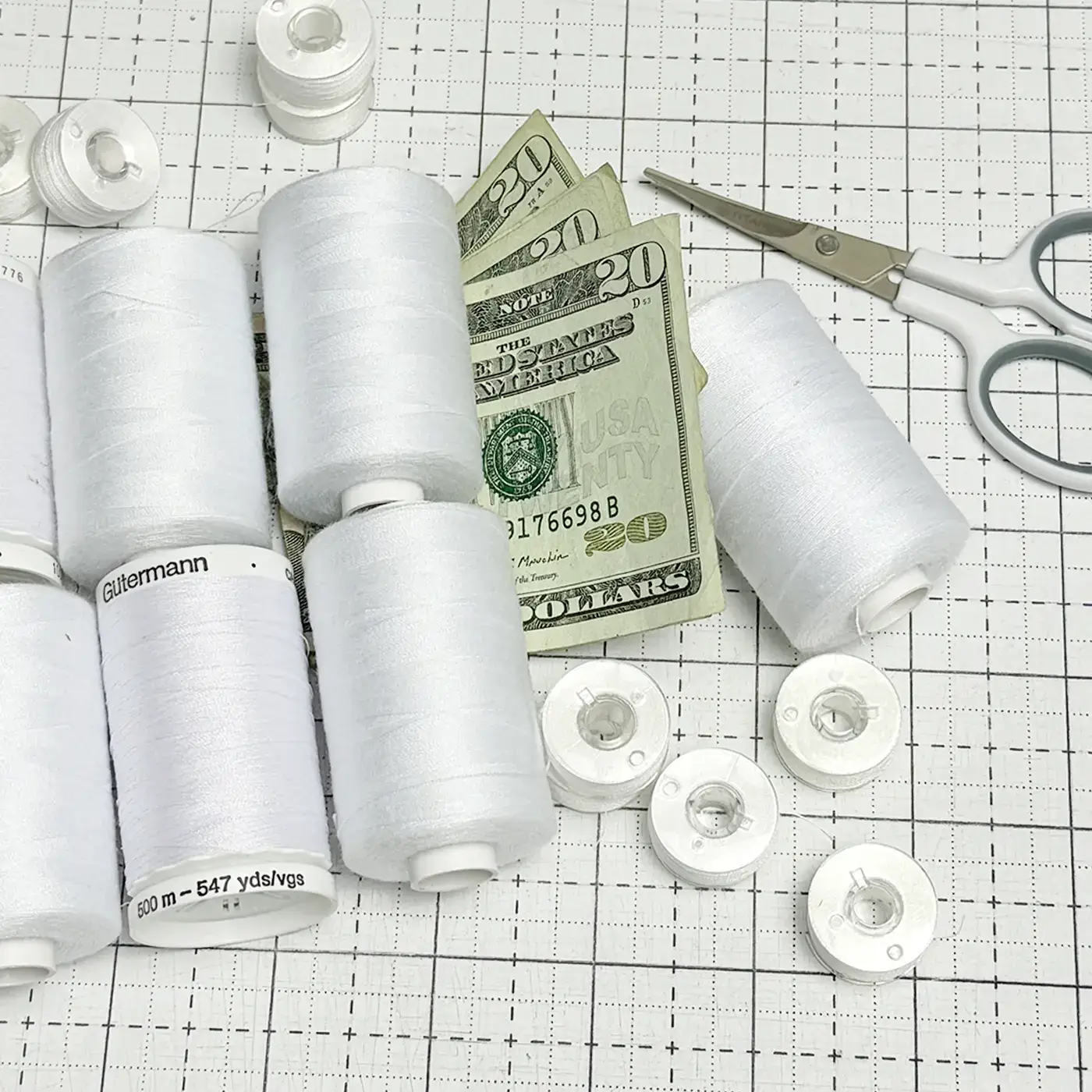 white thread, bobbins, scissors and money