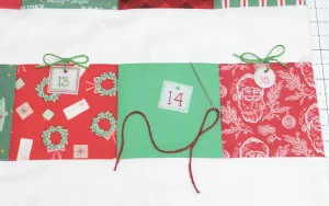 Close-up of a handmade fabric Advent calendar with numbered Christmas pockets. Shrink plastic number tags are tied onto the pockets with green and red twine for a festive, handmade look.