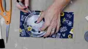 Hands tracing around a clear glass plate on navy sunflower fabric